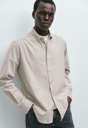 Beige overhemd met knopen gemaakt van zachte stof, met een klassieke kraag en lange mouwen, gecombineerd met donkergrijze jeans. Eenvoudig ontwerp en textuur.