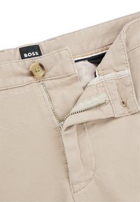 Pantalones de algodón beige con cierre de cremallera y botón, con una textura suave y detalles de costura visibles. Etiqueta de la marca "BOSS" adjunta.