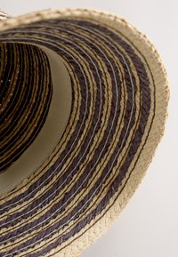 Pălărie de paie cu boruri largi, având benzile concentrice împletite în alternanță de culori închise și deschise, văzută din interior pe un fundal alb.