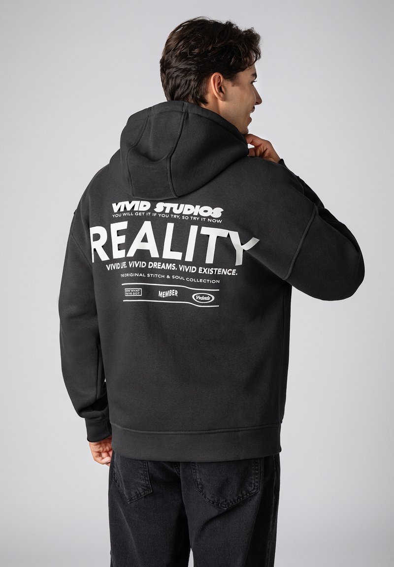 Black hooded sweatshirt featuring white printed text on the back, including "VIVID STUDIOS" and "REALITY," with a relaxed fit and soft texture.