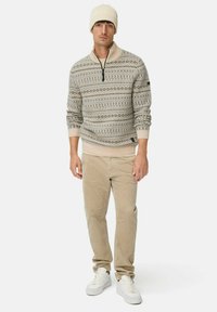 Beige gebreide pullover met een half-rits kraag, geometrische patronen, geribbelde manchetten, gecombineerd met lichtbeige corduroy broeken en witte sneakers.