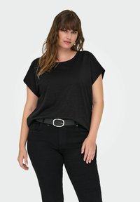 Svart kortärmad topp med avslappnad passform, rundad halsringning och subtil lyster, tillsammans med svarta jeans och ett tunt bälte.