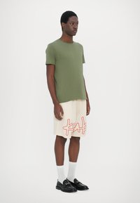 Olivengrøn kortærmet t-shirt, beige shorts med rødt abstrakt mønster, sorte loafers og hvide mellemlange strømper. Glatte teksturer.