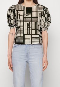 Blusa recortada hecha de tejido ligero, con mangas abullonadas, un escote redondo y un patrón geométrico abstracto en negro y crema.