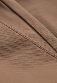 Gros plan sur un tissu marron texturé montrant une couture fine le long d'une couture et un détail plié.