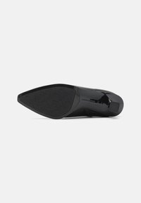 Pantof apare din piele lacuită neagră cu vârful ascuțit și o talpă din cauciuc texturat. Dispune de un toc scăzut, robust și accente de design minimaliste.