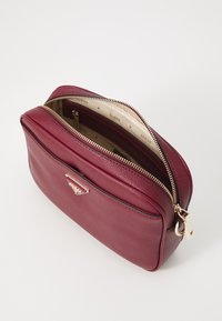 Borsa in pelle bordeaux con hardware dorato, chiusura con zip e interno con motivo logo. Forma rettangolare con una texture liscia e un design strutturato.