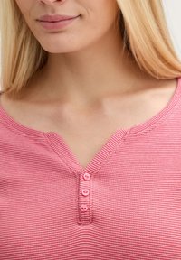 Haut à manches courtes rayé rose avec un décolleté en V, présentant quatre boutons assortis et un tissu doux et texturé.