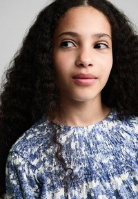 Een top met blauwe bloemenpatronen op een witte achtergrond, met een geplooide textuur rond de halslijn en van een zachte, lichte stof.