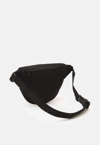 Borsa a tracolla nera in tessuto con chiusura a zip, forma curva, tracolla regolabile e texture liscia. Design minimalista senza logo visibili.