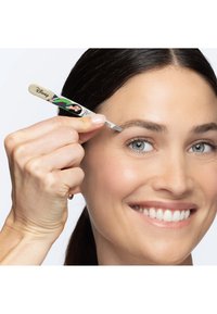 Femme souriante en train de façonner ses sourcils avec des pinces à épiler sur le thème de Disney, sur fond blanc.