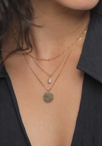 Kultaiset kerrokselliset kaulakorut, joissa on pyöreä riipus kimaltelevalla tekstuurilla ja pisaranmuotoinen koriste. Ketjut ovat ohuita ja hienostuneita.