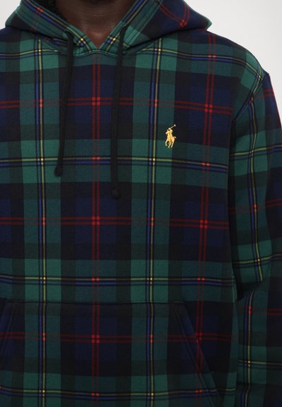 Uomo che indossa un felpa con cappuccio a scacchi verde, blu navy e rosso, con coulisse nera e logo del giocatore di polo ricamato giallo sul petto.