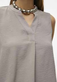 Top senza maniche grigio chiaro con scollatura a V, caratterizzato da un tessuto testurizzato e una vestibilità rilassata; abbinato a una collana con perle sferiche argentate.