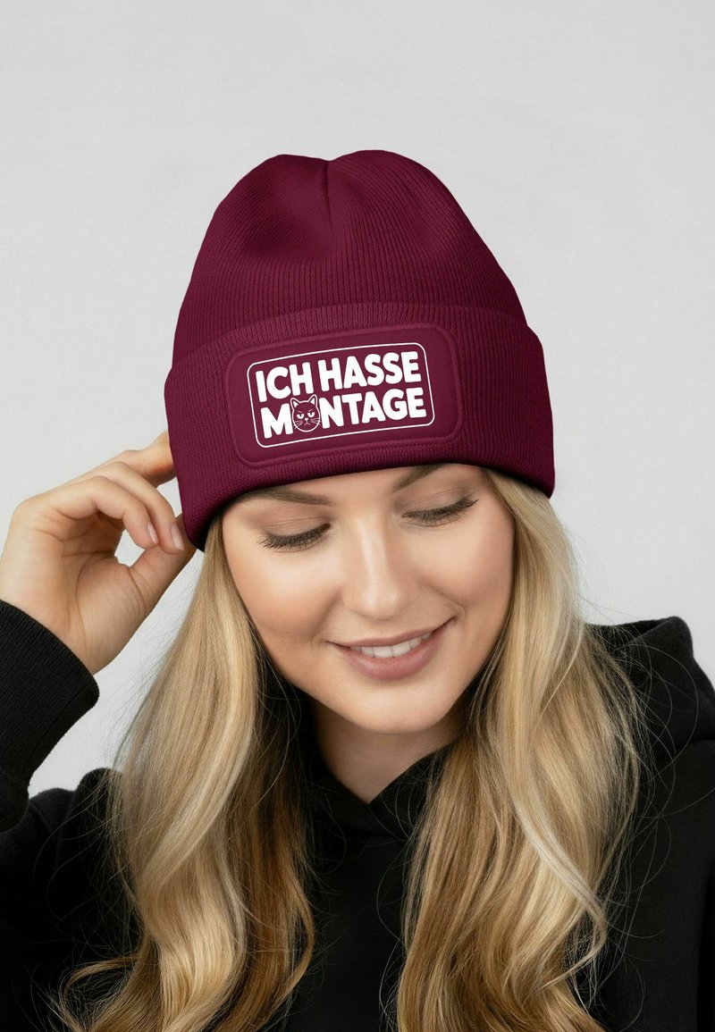Maroon beanie with ribbed texture, featuring a rectangular white patch that reads "ICH HASSE MONTAGE" with a cat illustration.