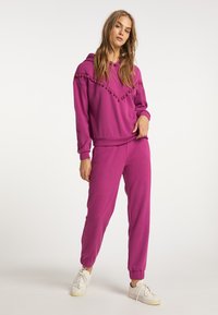 Felpa fucsia con dettagli a pompon, abbinata a joggers coordinati. Realizzata in materiale morbido, presenta polsini a coste e una vestibilità comoda.
