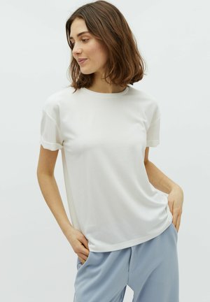 T-shirt blanc à manches courtes avec un col rond, présentant une texture lisse et une coupe décontractée, associé à un pantalon bleu clair.