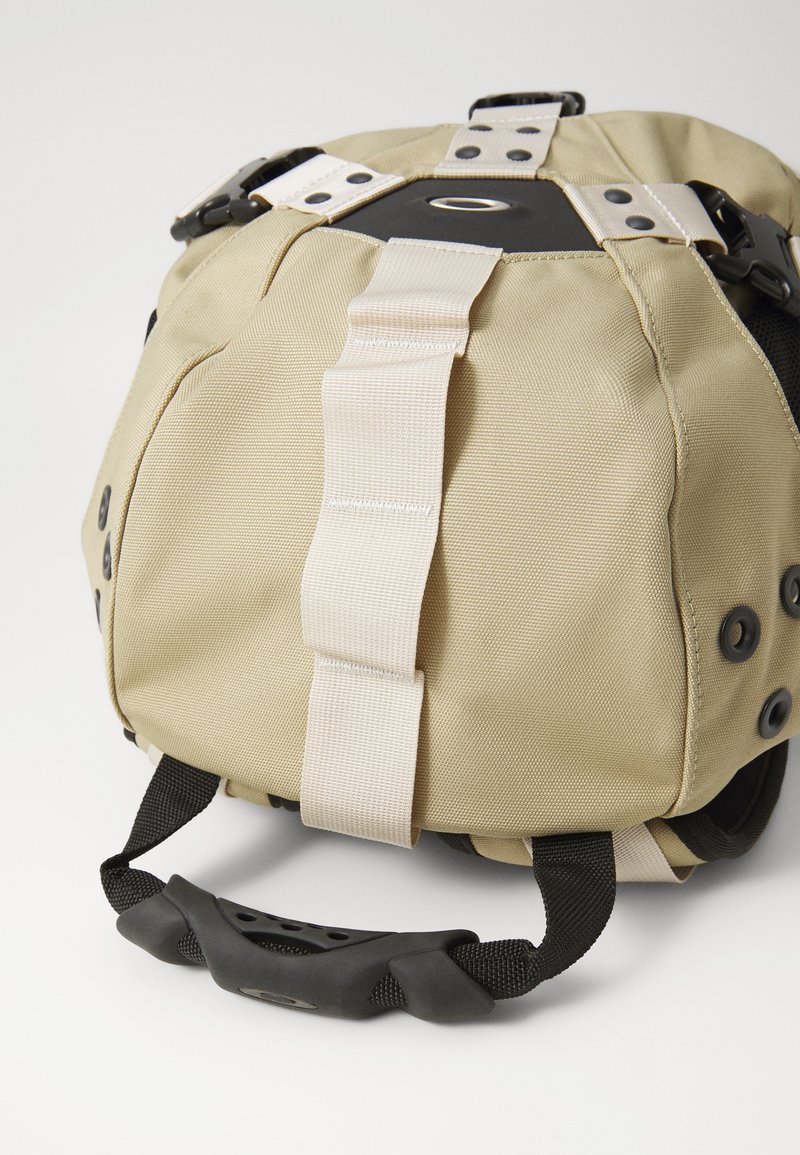 Beige Stofftasche mit schwarzen Akzenten, ausgestattet mit einer strukturierten Oberfläche, verstellbaren Trägern und einem gummierten Griff für besseren Halt.