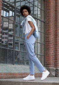Ljusblå skräddarsydda byxor kombinerade med en vit T-shirt och en ljusblå tröja över axeln. Vita sneakers fulländar looken.