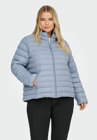Světle modrá péřová bunda s prošívan�ým vzorem, vysokým límcem, předním zipem a bočními kapsami. Měkký materiál s volným střihem.