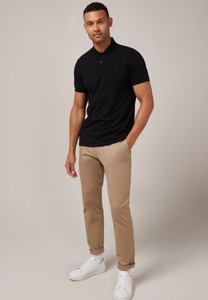 Zwarte poloshirt met korte mouwen, gecombineerd met beige chino's. Schoenen zijn witte sneakers met een gestructureerde zool.