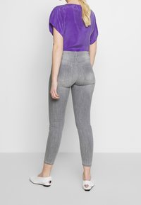 Grå högmidjade jeans med en subtil textur. Kombination med en lila topp med korta ärmar och en slät yta. Vita slip-on skor.