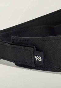 Czarny pasek wykonany z teksturowanej tkaniny, z wyraźną metką z logo Y-3 w kontrastującym białym kolorze. Design jest elegancki i minimalistyczny.