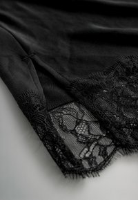 Black garment with a smooth texture, featuring a lace hem with intricate floral patterns. The edges are raw and slightly frayed.