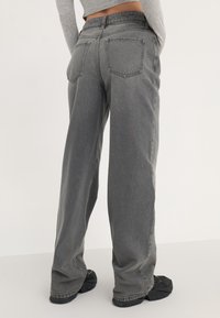 Vaqueros de pierna ancha en gris hechos de mezclilla, con cintura alta, bolsillos traseros y bajos doblados, combinados con calzado negro texturizado.