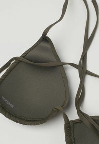 Trojúhelníkový horní díl bikin olivově zelené barvy s tenkými nastavitelnými šňůrkami a jemně prošitými okraji na světlém pozadí.
