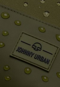 Textúrált világoszöld tok vízcseppekkel, melyen egy téglalap alakú fehér címke található, melyen purple betűkkel van feltüntetve a "JOHNNY URBAN" felirat.