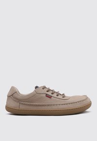 Zapatilla de cuero beige con un perfil bajo, puntera redonda y diseño de cordones. Suela de goma texturizada y costura lateral con un sutil detalle de logo.