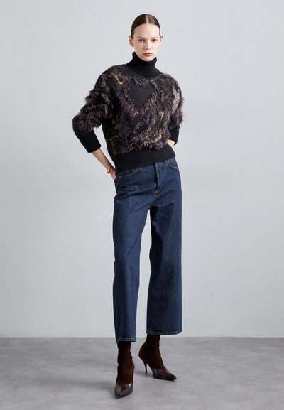 Pulover negru și violet cu un model decorat, cu detalii de franjuri, asortat cu pantaloni din denim închis, cu talie înaltă și cizme cu toc de culoare maro.