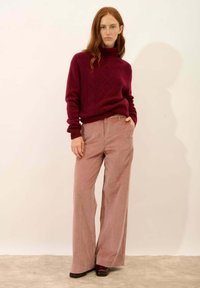 Suéter de cuello alto de punto burdeos con un patrón texturizado, combinado con pantalones de pana de pierna ancha en rosa claro y zapatos oscuros.