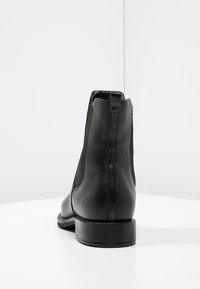 Botas de tobillo de cuero negro con una textura suave, paneles laterales elásticos y punta redondeada, con un tacón bajo y un diseño minimalista.