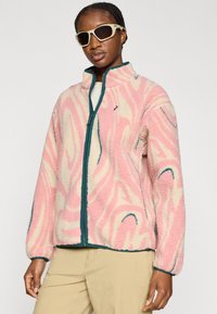 Μπουφάν από φλις με ροζ και κρεμ στροβιλιζόμενο σχέδιο και τιρκουάζ λεπτομέρειες, γιακά που στέκεται και κλείσιμο με φερμουάρ μπροστά.