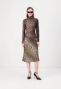 Leopard print fitted long-sleeve top with high neck, paired with a flowing leopard print midi skirt. Black heeled shoes complete the look.