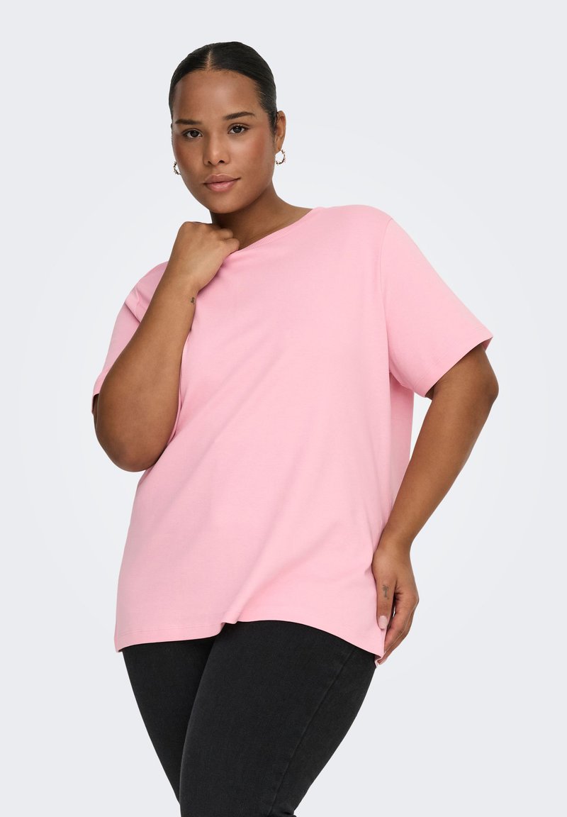 Lyserød bomulds t-shirt med løs pasform, korte ærmer og rund halsudskæring. Kombineret med sorte jeans, der har en glat tekstur.