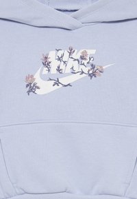 Ανοιχτό μπλε φούτερ με λευκό λογότυπο Nike και λουλούδια κεντημένα σε ροζ και μωβ. Το υλικό φαίνεται μαλακό με καγκουρό τσέπη.