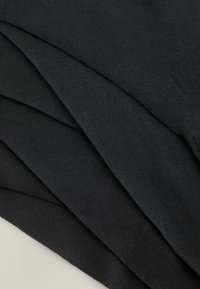 Material negru pliat ordonat, cu o textură netedă și un model subtil de dungi. Materialul pare moale și elastic.