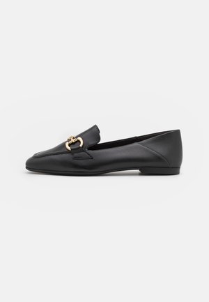 Mocassin plat en cuir noir avec bout arrondi et détail en métal doré en forme de mors de cheval sur le dessus, présenté sur un fond blanc uni.