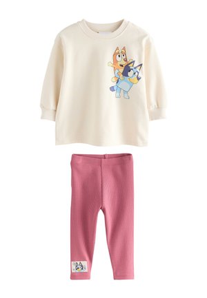 Barn med blondt hår i en lav knold iført en cremefarvet sweatshirt med et farverigt Bluey tegneseriehund-design på ryggen.