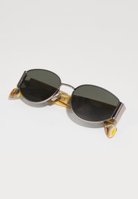 Ochelari de soare rotunzi cu lentile întunecate, cadru din metal argintiu și brațe cu un model marmorat galben și portocaliu. Ușori, cu un design elegant.