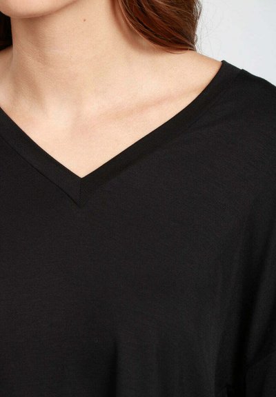 T-shirt nera a V in tessuto morbido, caratterizzata da una vestibilità rilassata e una texture liscia. Il collo ha un bordo pulito e in linea con il design.
