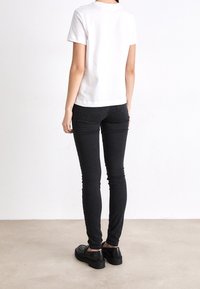 Camiseta de algodón blanca con mangas cortas, combinada con jeans ajustados negros. El calzado son unos zapatos de plataforma negros con un acabado texturizado.