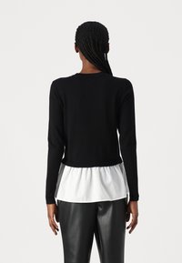 Czarny sweter wykonany z dzianiny, z długimi rękawami, z białym, warstwowym wykończeniem u dołu. Materiał wydaje się miękki; skrócony krój z dopasowanym wcięciem w talii i teksturowanym materiałem.