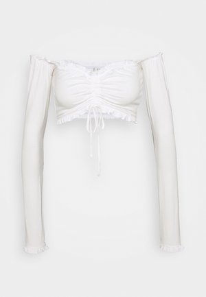 Crop top blanc épaules dénudées avec manches longues, devant froncé, cordon de serrage et volant décoratif sur l'encolure, l'ourlet et les poignets.