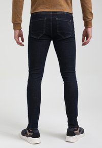 Mörkblå tajta jeans har en klassisk 5-ficksdesign, slät textur och subtila sömnadsdetaljer. Bärs med sportiga svarta och grå sneakers.