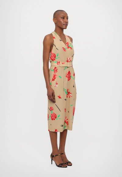 Rochie bej cu modele florale roșii și verzi, fără mâneci, cu decolteu în V, talie accesorizată cu centură și lungime midi. Sandale negre cu toc înalt.
