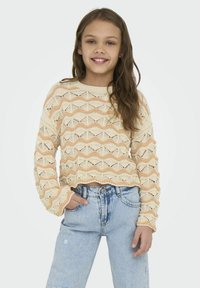 Gehaakte pullover met golvenpatroon in room- en perzikkleuren, lange mouwen, relaxte pasvorm, gecombineerd met lichtblauwe high-waisted jeans.
